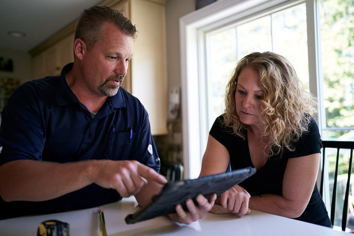 A contractor walking a homeowner through a quote on a tablet at her kitchen table
